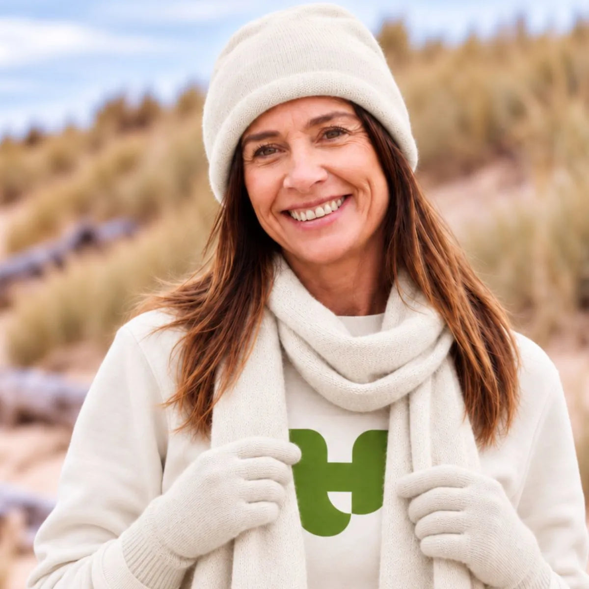 Femme souriante portant un bonnet, une écharpe et des gants en cachemire et laine Sable Vercors, dans les dunes – PALÂBA