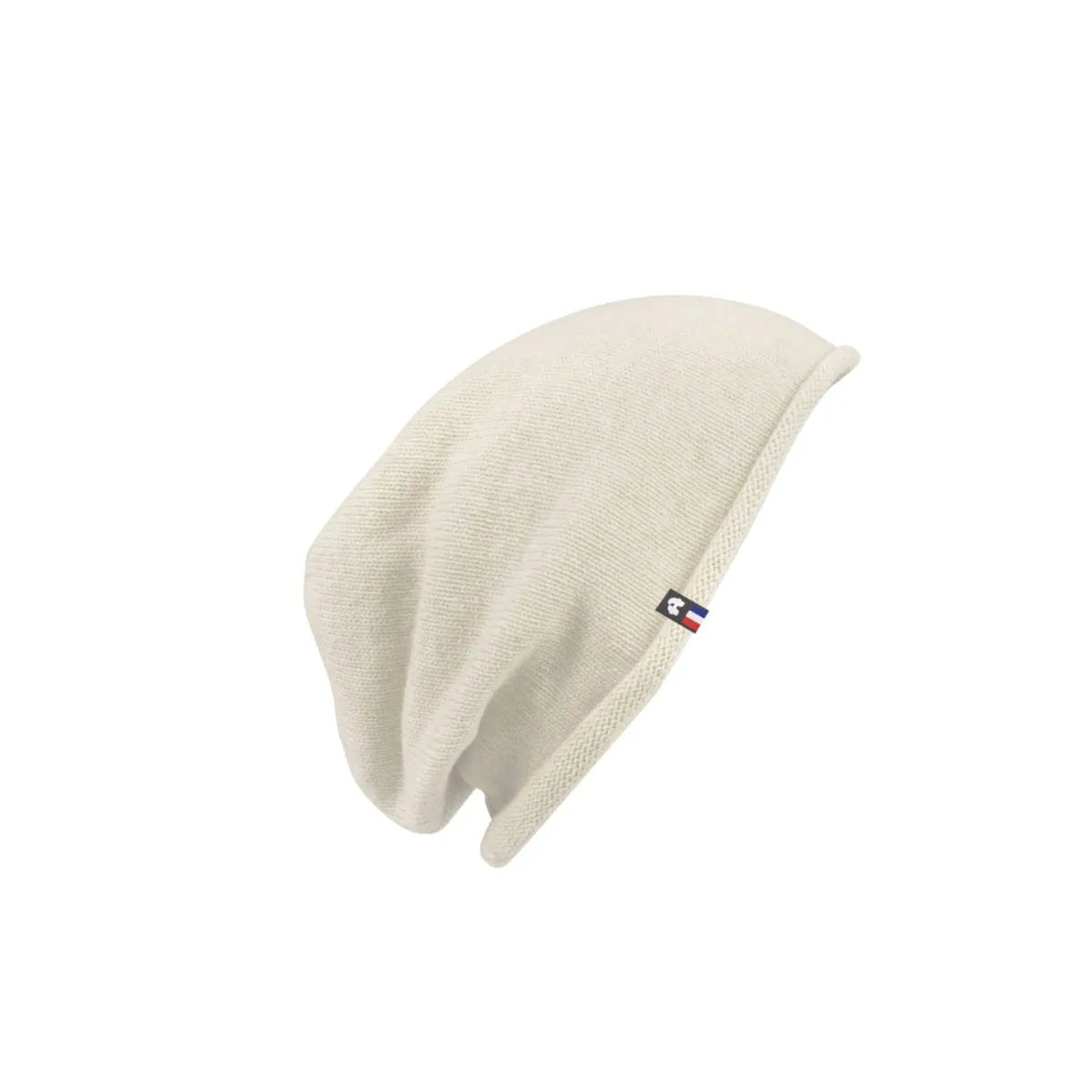 Bonnet tombant en cachemire et laine Sable Vercors à bord roulotté et étiquette tricolore, posé à plat – PALÂBA