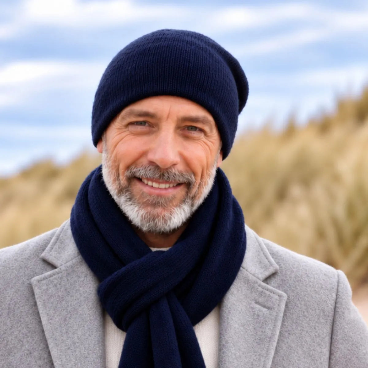 Homme barbu portant un bonnet et une écharpe en cachemire et laine Marine Léman, manteau gris, dans les dunes – PALÂBA