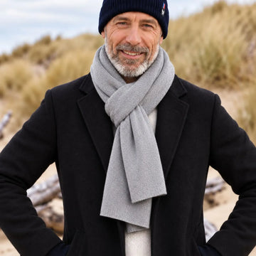 Homme barbu portant une écharpe en cachemire et laine Gris Gavarnie nouée sur un manteau noir, dans les dunes – PALÂBA