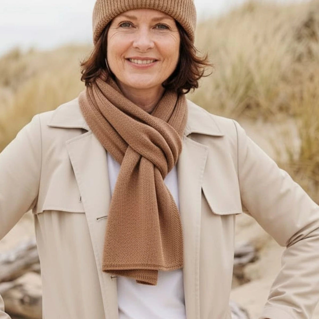 Femme souriante portant une écharpe en laine mérinos Camel Aubrac et le bonnet assorti, dans les dunes – PALÂBA