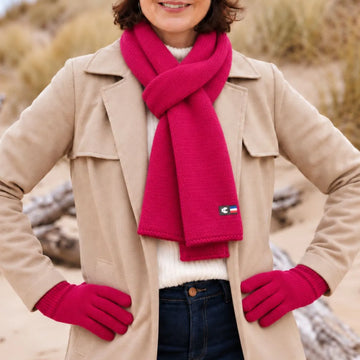 Femme en manteau beige portant une écharpe en laine mérinos Fuchsia Rosière nouée et les gants assortis, sur la plage – PALÂBA