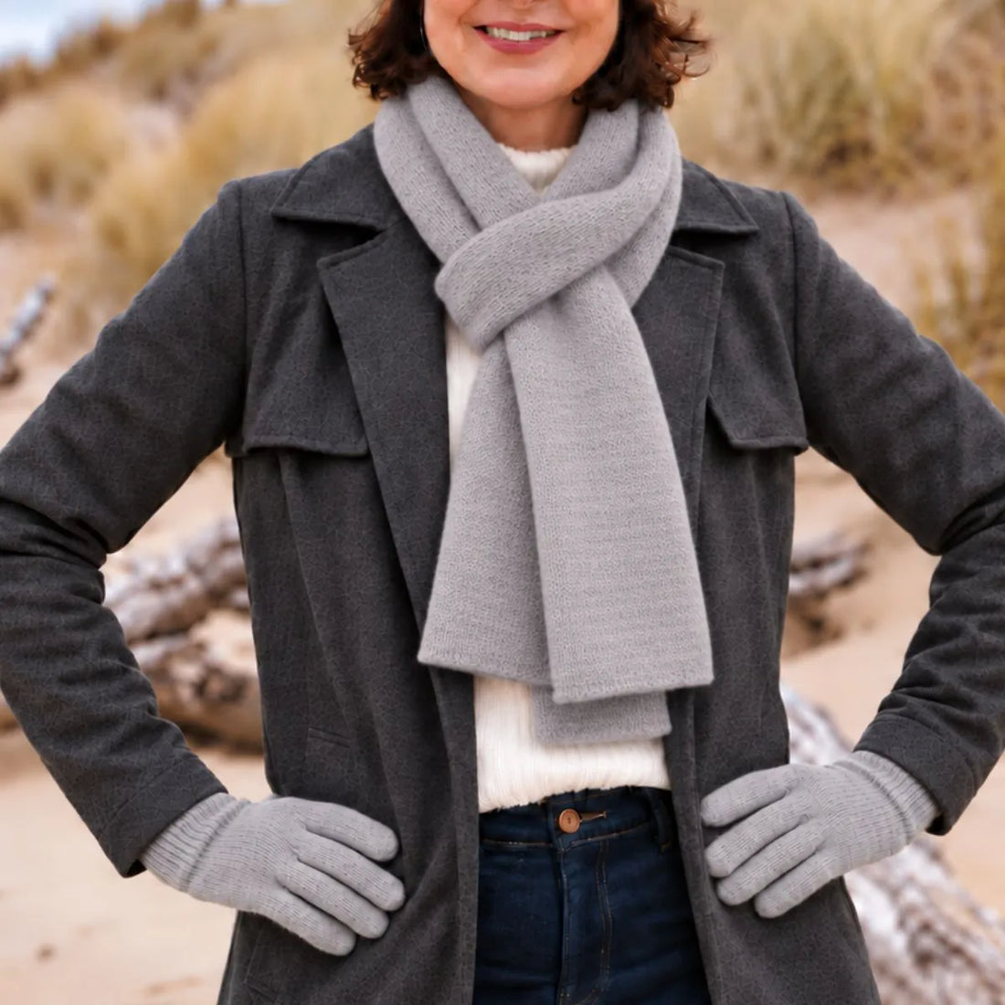 Femme en manteau anthracite portant une écharpe en laine mérinos Gris Gavarnie nouée et les gants gris assortis, sur la plage – PALÂBA