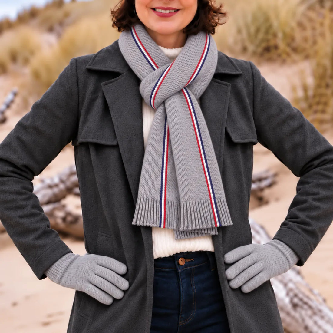 Femme en manteau anthracite portant une écharpe tricolore grise à franges et des gants gris, sur la plage – PALÂBA