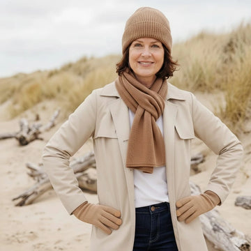 Femme portant l'ensemble bonnet, écharpe et gants en laine mérinos Camel Aubrac dans les dunes en bord de mer – PALÂBA