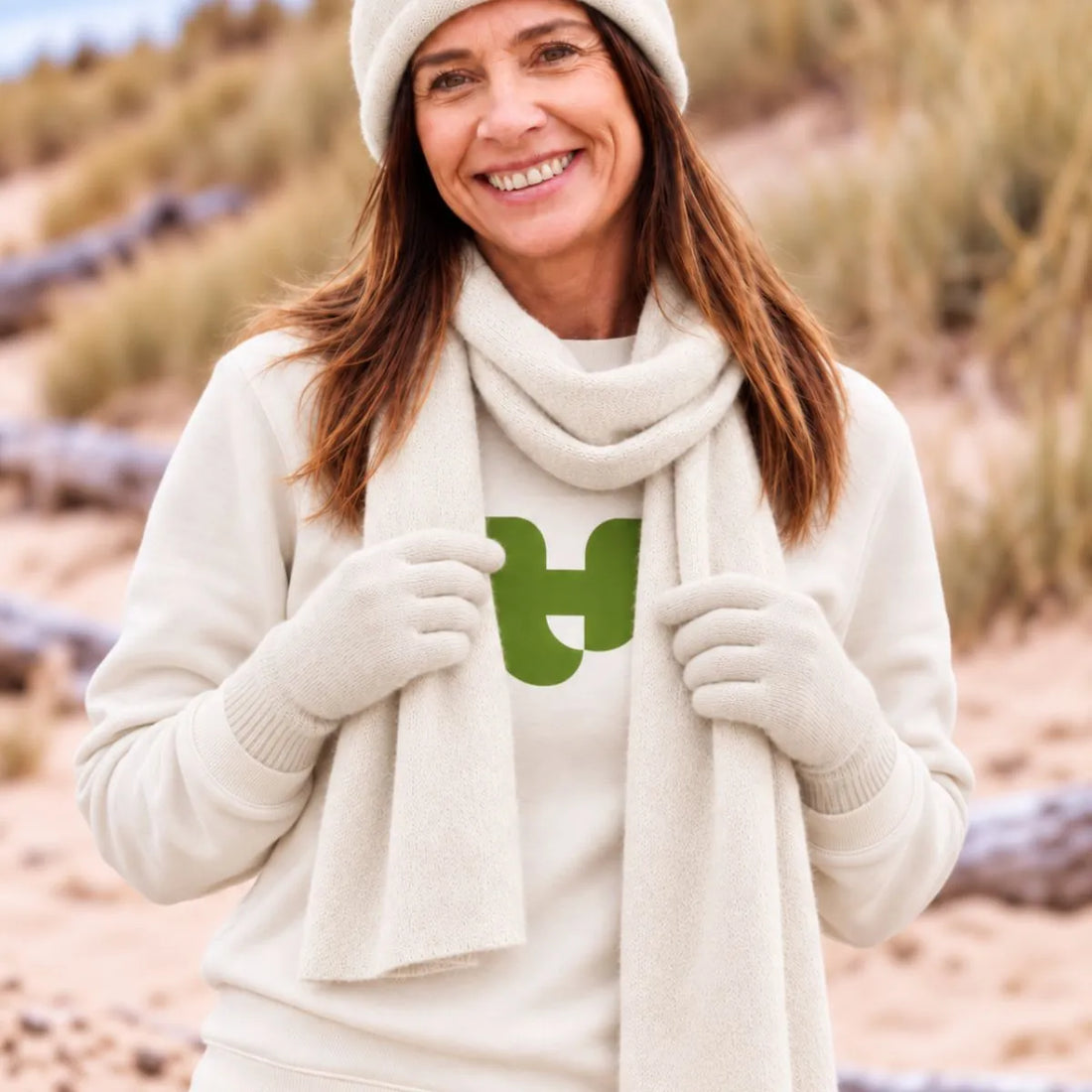 Femme portant le bonnet, l'écharpe et les gants en cachemire et laine Sable Vercors sur un sweat écru, dans les dunes – PALÂBA