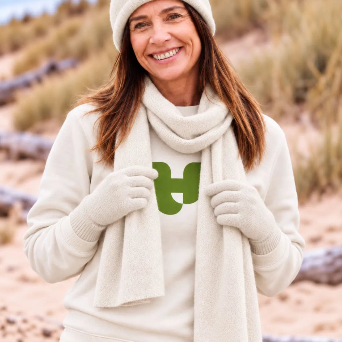 Femme portant le bonnet, l'écharpe et les gants en cachemire et laine Sable Vercors sur un sweat écru, dans les dunes – PALÂBA