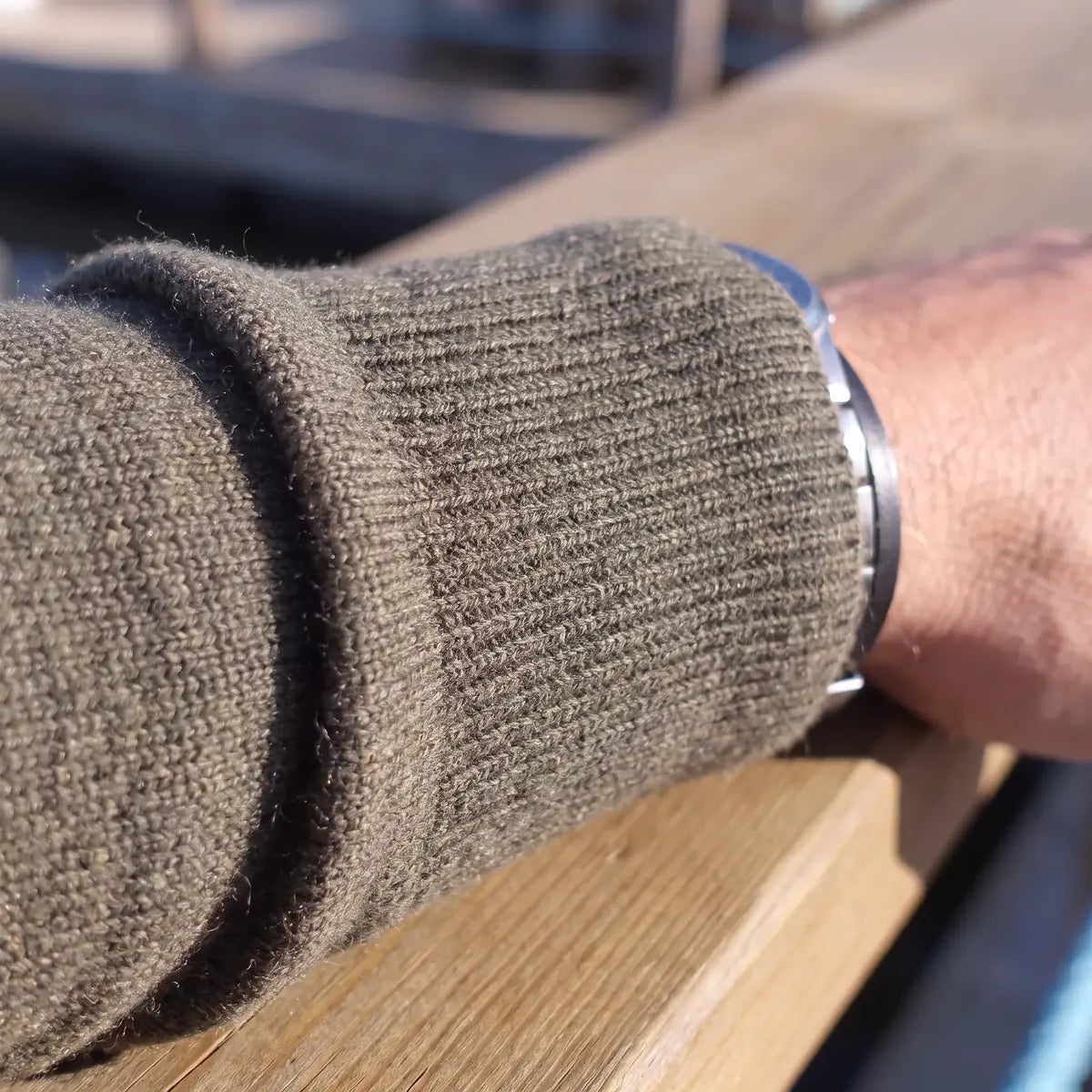 Poignet en bord-côte du pull kaki en laine mérinos posé sur une rambarde en bois – PALÂBA