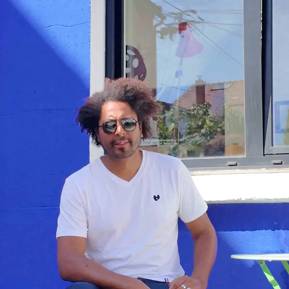 Homme portant le t-shirt col V blanc en coton bio et des lunettes de soleil, devant un mur bleu – PALÂBA
