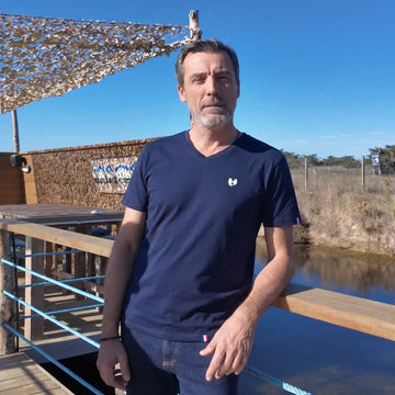 Homme portant le t-shirt col V bleu marine avec un jean brut, sur un ponton au bord de l'eau – PALÂBA